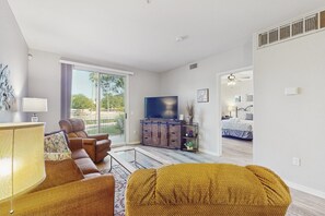 A modern living room with a sofa, armchair, and ottoman, a television, and a sliding glass door leading to a balcony.
