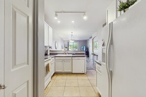 A modern kitchen with white cabinetry, a central island, and a view to the outdoors.