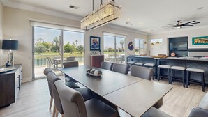 Un comedor amplio con una mesa larga y sillas, una araña y vistas al exterior.
