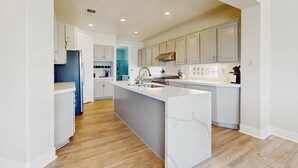 Una cocina moderna con una isla central, suelo de madera y muebles de color claro.