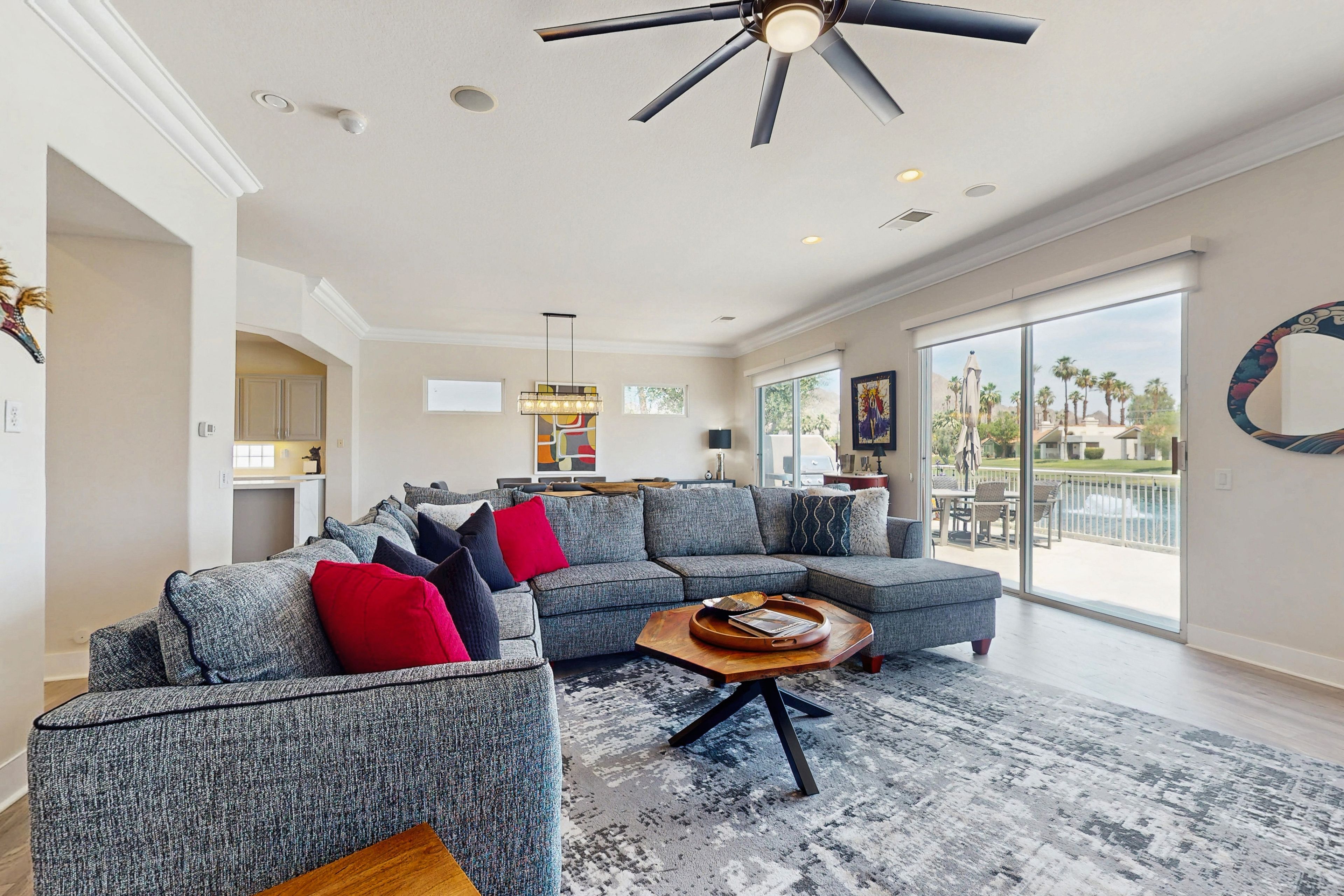 A spacious living room with a large gray sectional sofa, a wooden coffee table, and a ceiling fan.