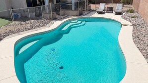 A swimming pool with a curved edge, surrounded by a pebble border and a fence. - Sun-filled dog-friendly home with private pool, putting green, & mountain views (Tucson)