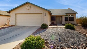 A single-story house with a garage, a front porch, and a landscaped driveway. - Sun-filled dog-friendly home with private pool, putting green, & mountain views (Tucson)