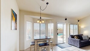 A living room with a sofa, a dining table with chairs, a chandelier, and a painting on the wall. - Sun-filled dog-friendly home with private pool, putting green, & mountain views (Tucson)