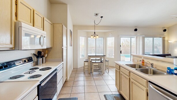 A kitchen with a stove, microwave, and sink, wooden cabinets, and a dining area with a table and chairs. - Sun-filled dog-friendly home with private pool, putting green, & mountain views (Tucson)