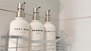 Un estante de baño con tres botellas que contienen jabón corporal, champú y acondicionador.