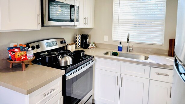 Cocina compacta con gabinetes blancos, microondas, estufa y pileta.