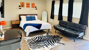 Un dormitorio con una cama, un sofá de cuero, un tapete de cebra y obras de arte en la pared.
