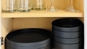 Una estantería de madera con cristalería transparente y platos negros.