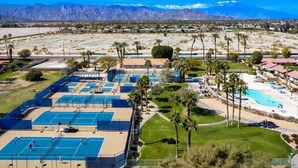 Complejo de canchas de tenis con varias canchas, una zona de piscina y palmeras.