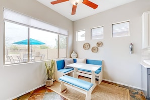A room with a white ceiling fan, a large window with blinds, a blue bench, a white table, and a fire extinguisher on the wall. - Inviting, dog-friendly home with pool, enclosed yard, firepit & fast WiFi (Phoenix)