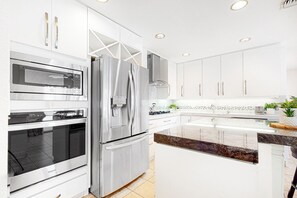 A modern kitchen with stainless steel appliances, white cabinetry, and a granite countertop. - Serene, dog-friendly home w/ private pool, spa & grill - close to El Paseo (Palm Desert)