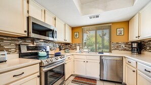 A modern kitchen with stainless steel appliances, white cabinetry, and a patterned backsplash.