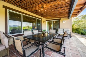 Um pátio externo com mesa de vidro, cadeiras de vime e teto de madeira.