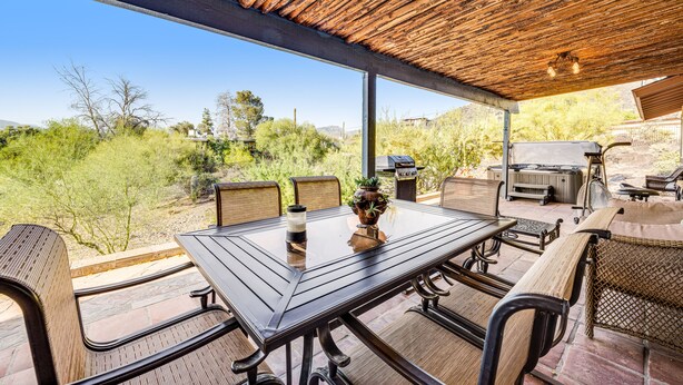 An outdoor patio with a wooden table and chairs, a grill, and a view of the surrounding landscape.