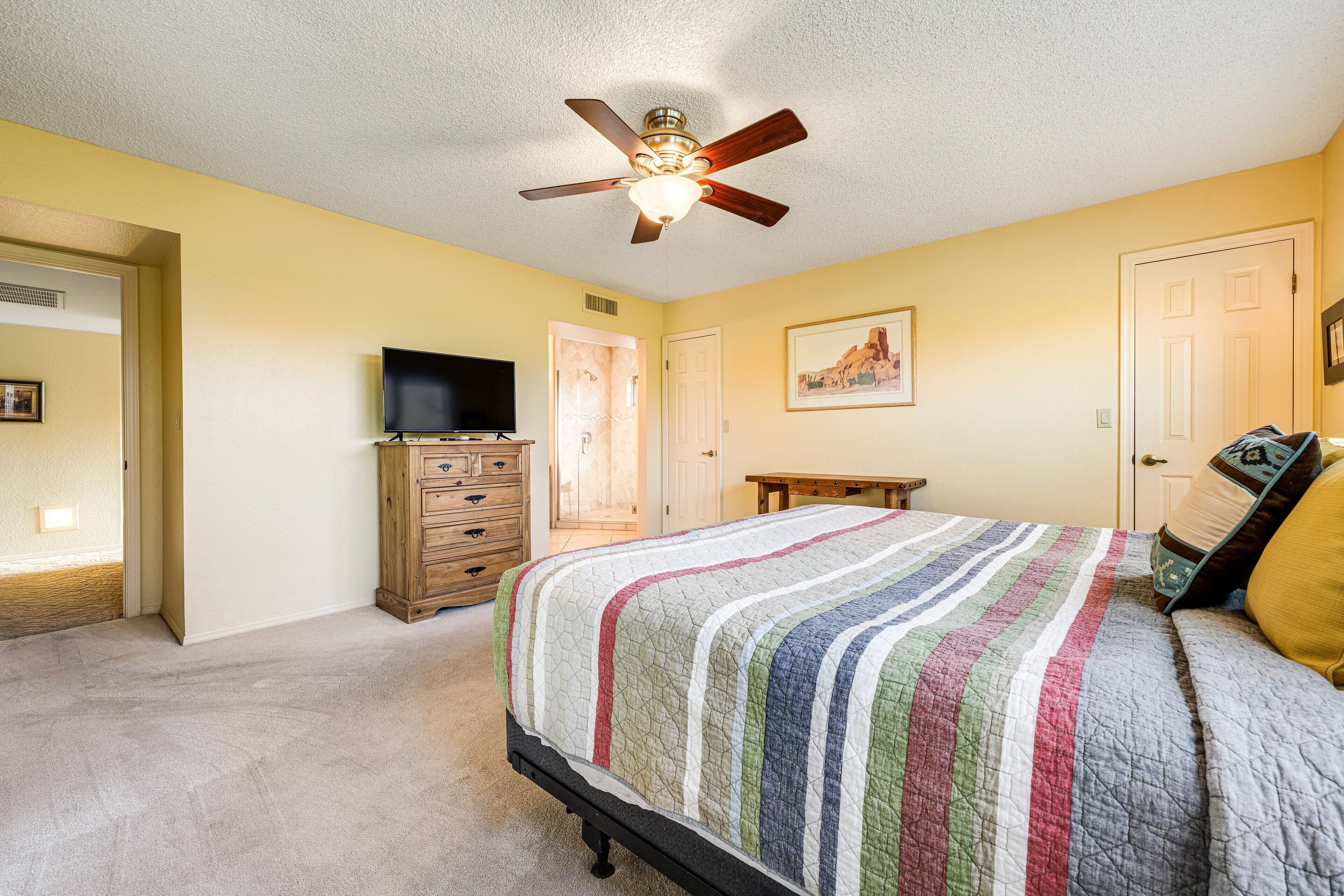 Une chambre à coucher avec un lit, un ventilateur de plafond, une commode, un téléviseur et une porte.
