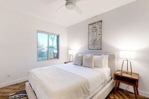 Ein Schlafzimmer mit einem Bett, einem Fenster, einem Wandbild und einem Nachttisch mit einer Lampe.