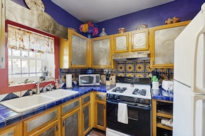 A kitchen with blue and yellow patterned tiles, wooden cabinets, a white sink, a black stove, and a microwave.