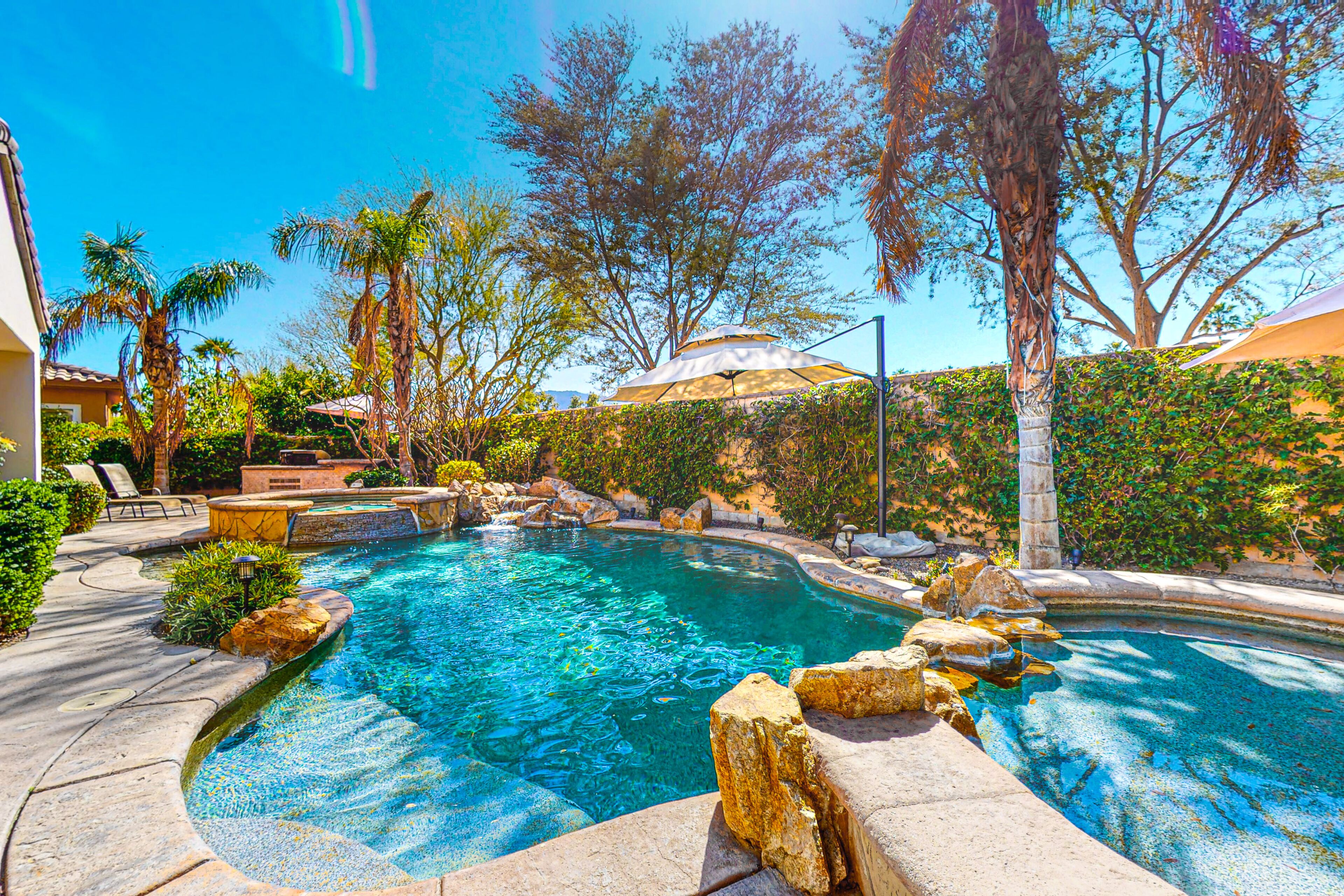 A swimming pool with clear blue water, surrounded by rocks and palm trees.