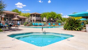 A swimming pool with lounge chairs and umbrellas, surrounded by buildings with a tiled roof. - Dog-friendly condo with high-speed WiFi, heated outdoor pool & hot tub (Oro Valley)