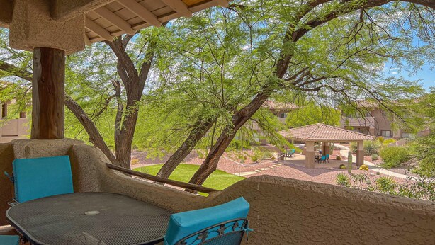 A covered outdoor seating area with a table and chairs, overlooking a courtyard with trees and a building. - Dog-friendly condo with high-speed WiFi, heated outdoor pool & hot tub (Oro Valley)