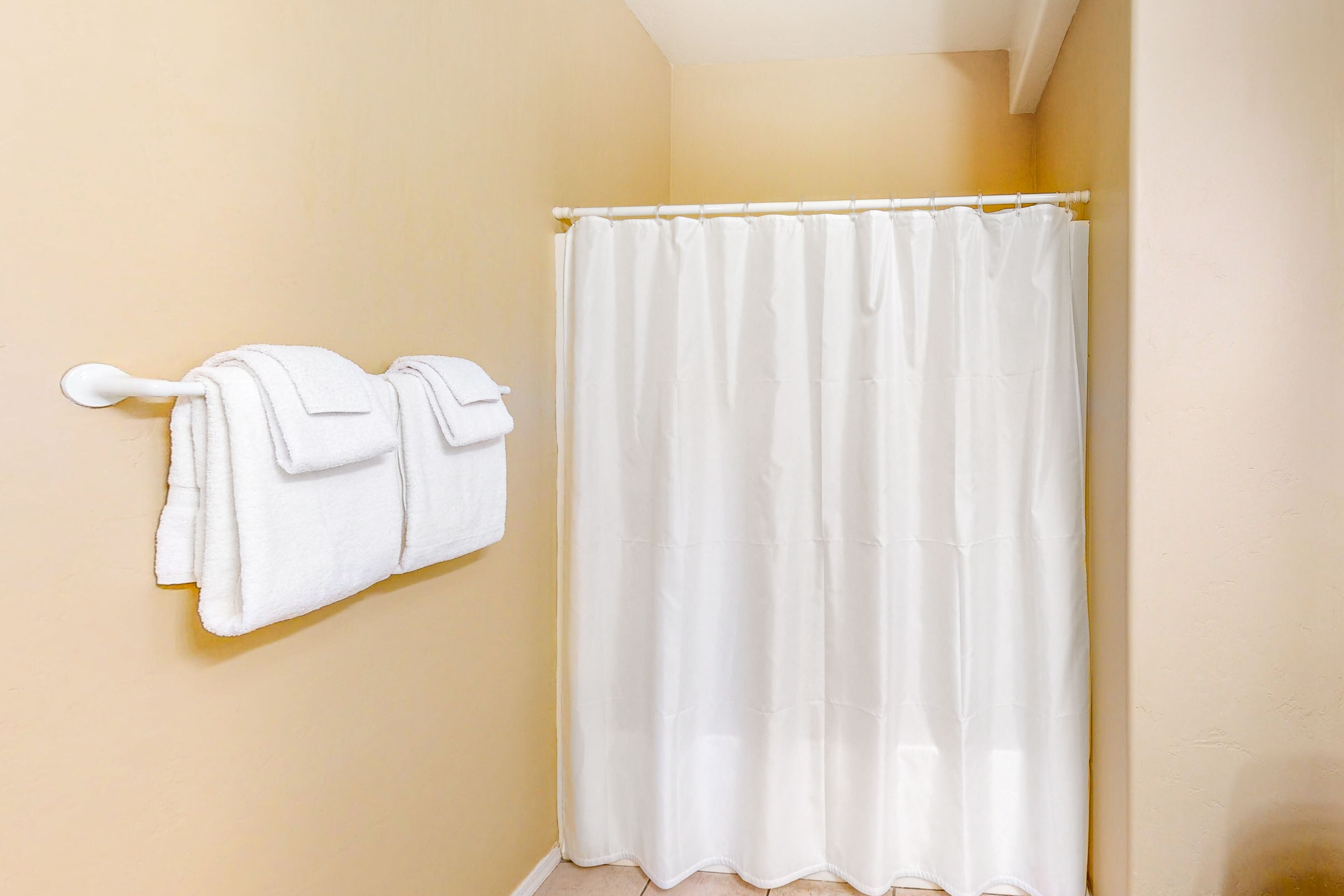 Une salle de bain avec un mur de couleur beige, un rideau de douche blanc et deux serviettes blanches suspendues à un porte-serviettes.