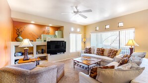 A living room with a sofa, armchair, coffee table, TV, and decorative items. - Dog-friendly condo with high-speed WiFi, heated outdoor pool & hot tub (Oro Valley)
