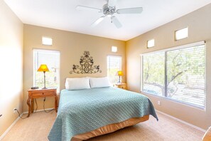 Un dormitorio con una cama, dos lámparas de noche, un ventilador de techo y dos ventanas con persianas.