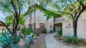 A building with a number '16' on the wall, a paved walkway, and various desert plants. - Dog-friendly condo with high-speed WiFi, heated outdoor pool & hot tub (Oro Valley)