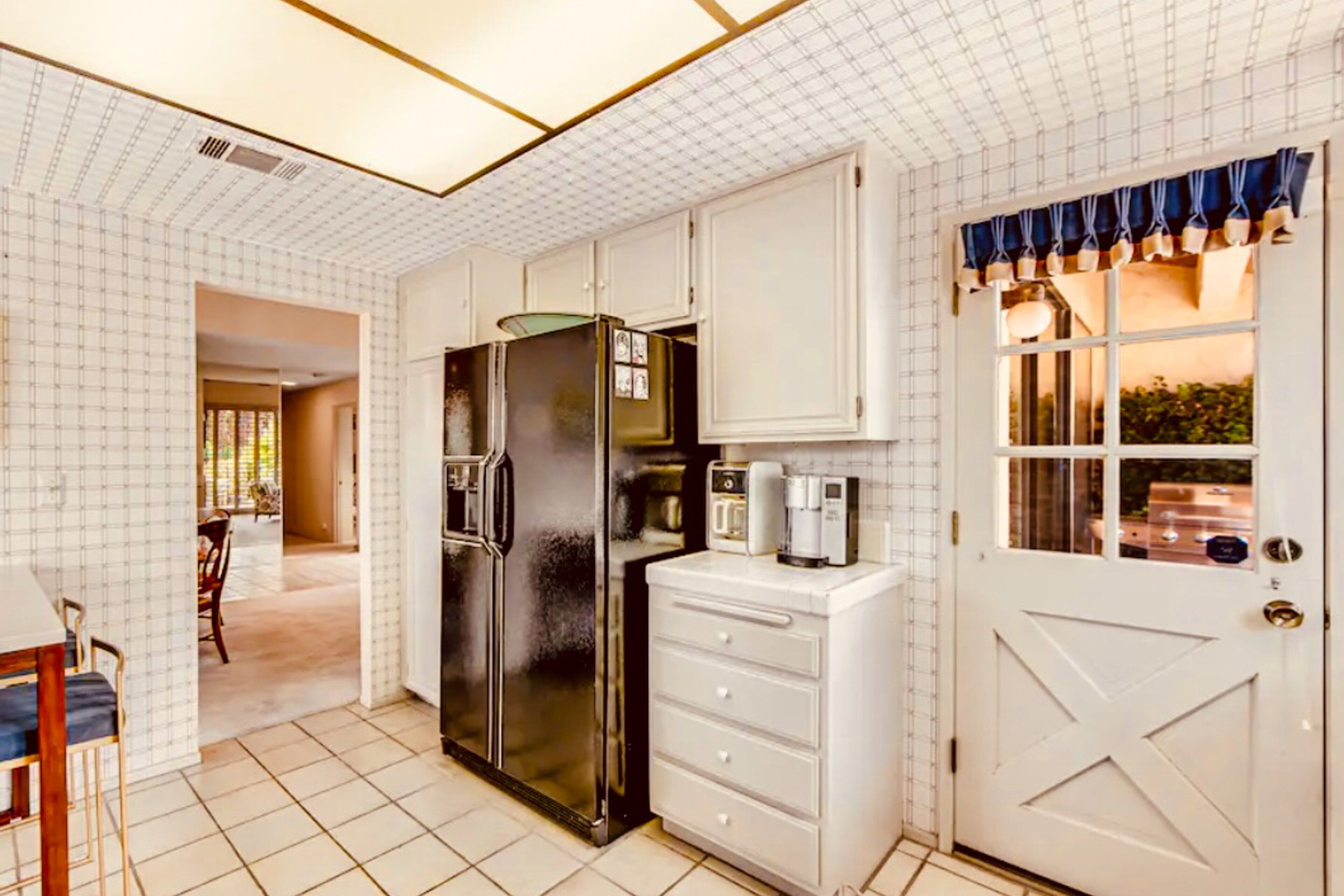 A kitchen with white cabinetry, a black refrigerator, a coffee maker, and a door with a window.