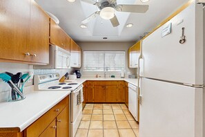 A compact kitchen with wooden cabinets, a white refrigerator, a stove, and a ceiling fan. - Large home w/ a full kitchen, furnished patio, & private, outdoor pool (Phoenix)