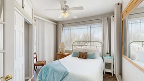 A bedroom with a bed, a nightstand, a chair, a window with blinds, and a ceiling fan. - Beautiful first-floor condo with pool, hot tub, & full kitchen - near hiking (Oro Valley)