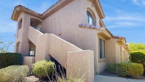 A stucco house with a prominent staircase, a small porch, and a well-maintained garden. - Beautiful first-floor condo with pool, hot tub, & full kitchen - near hiking (Oro Valley)