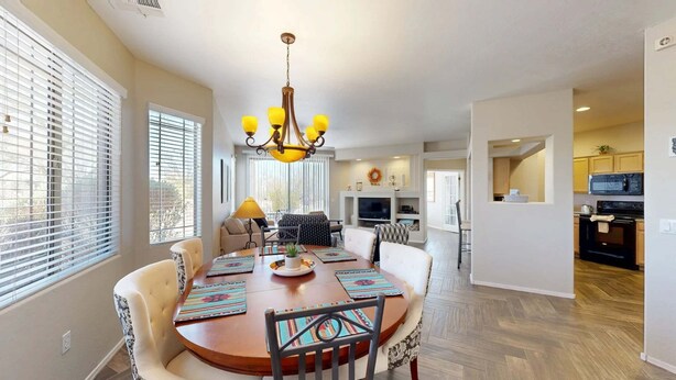 A dining area with a round table, chairs, a chandelier, and a kitchen in the background. - Beautiful first-floor condo with pool, hot tub, & full kitchen - near hiking (Oro Valley)