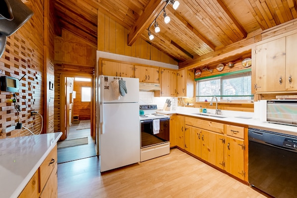 A modern kitchen with wooden cabinets, a white refrigerator, and a dishwasher. - Dog-friendly rustic retreat with enclosed yard, grill, wood stove, games, & W/D (Munds Park)