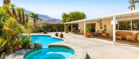 A backyard with a swimming pool, patio furniture, and a covered seating area.