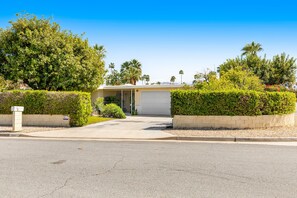 A residential driveway leading to a garage with a white garage door, surrounded by well-maintained hedges and palm trees. - Mountain view home with a pool, pool spa, grill, firepit, washer/dryer, and AC (Palm Springs)