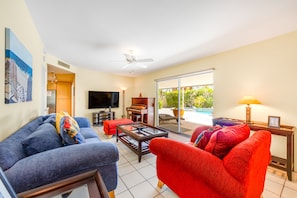A living room with a blue sofa, red sofa, and a piano. There is a television, a table, and a window with a view of greenery. - Mountain view home with a pool, pool spa, grill, firepit, washer/dryer, and AC (Palm Springs)