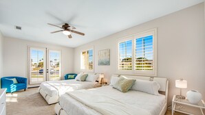 Un dormitorio con dos camas, un ventilador de techo y vistas al exterior a través de amplias ventanas.