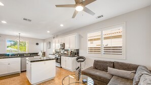 Una cocina moderna con armarios blancos, una isla central y un comedor con mesa de vidrio.