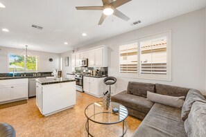 A modern kitchen with white cabinets, a central island, and a dining area with a glass table. - Dazzling retreat w/ a pool, grill, firepit, game room, & W/D - snowbird friendly (Indio)