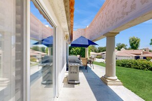 A covered outdoor patio with a grill, chairs, and umbrellas.