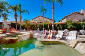 A pool area with lounge chairs, palm trees, and a building in the background. - Luxe and spacious retreat with a pool, pool spa, firepit, grill, game room, & AC (Indio)