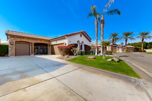 A single-story house with a garage, a well-maintained lawn, and palm trees. - Luxe and spacious retreat with a pool, pool spa, firepit, grill, game room, & AC (Indio)