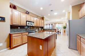 A spacious kitchen with wooden cabinets, granite countertops, a stainless steel refrigerator, and a built-in island. - Luxe and spacious retreat with a pool, pool spa, firepit, grill, game room, & AC (Indio)