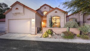 Una casa con garaje, entrada principal y un jardín bien cuidado con cactus y otras plantas propias del desierto.