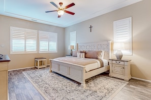 A bedroom with a bed, a nightstand, a lamp, a ceiling fan, and a cross on the wall. - Luxury home with an enclosed yard, pool, pool spa, & chef's kitchen - dogs ok (Palm Desert)
