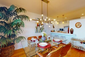 Un coin repas moderne avec une table en verre, des sets de table rouges et des plantes en osier.