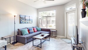 A living room with a sectional sofa, two coffee tables, a floor lamp, and a TV stand. - Inviting Condo w/ a Shared, Heated Pool, Hot Tub, Fitness Room & Sauna (Scottsdale)