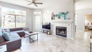 A modern living room with a fireplace, television, and a large window. - Inviting Condo w/ a Shared, Heated Pool, Hot Tub, Fitness Room & Sauna (Scottsdale)